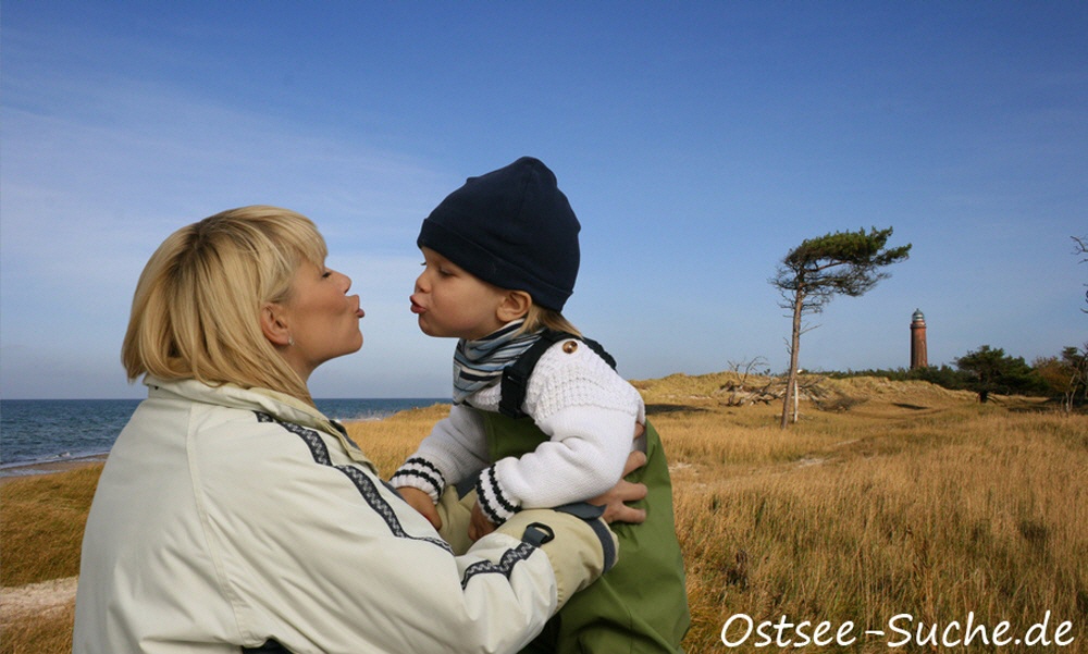 Mutter küsst ihr Kind vor dem Leuchtturm auf Rügen