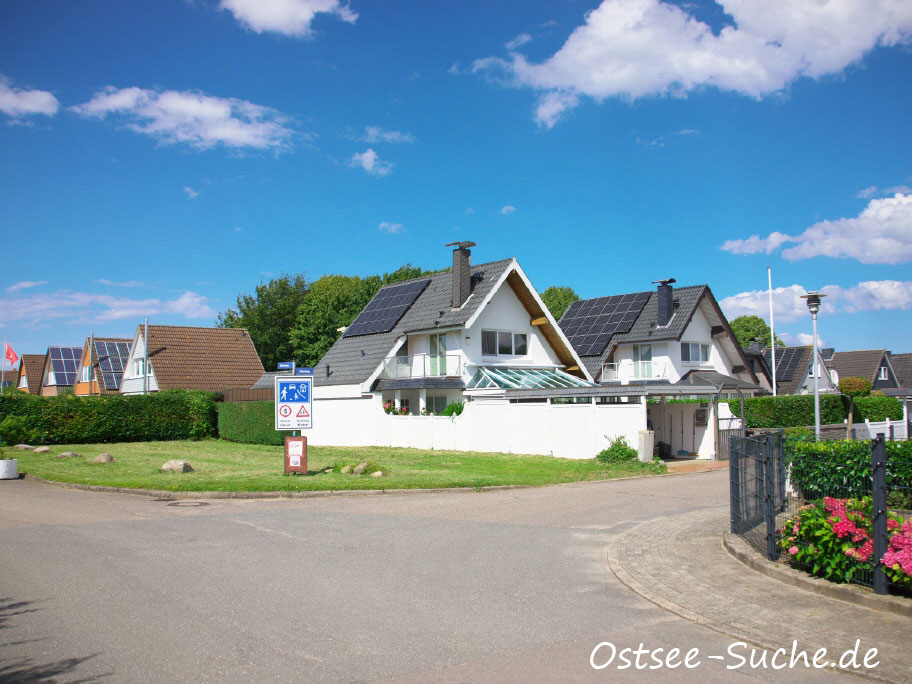 Zufahrt zur Ferienhaussiedlung am Kraksdorfer Strand. Ein weißes Ferienhaus steht in der Mitte des Bildes